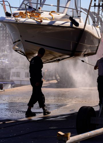 2 people pressure washing hanging boat in marina